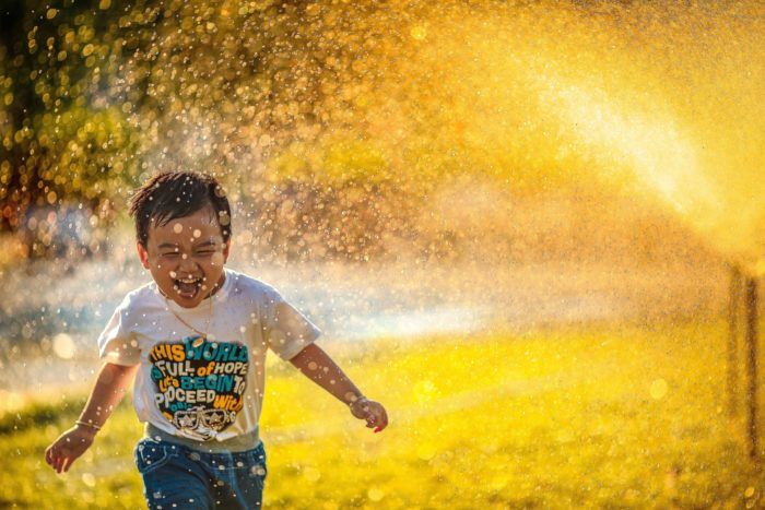 Happy child running in a sprinkler at sunset.