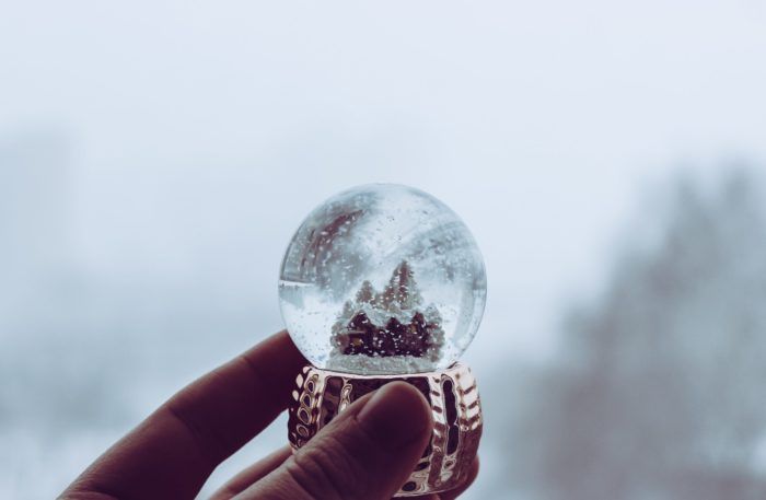 hand holding small snow globe with little houses and trees inside